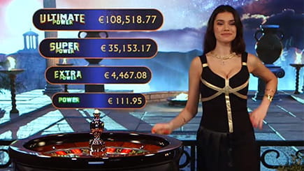 Ein Live Croupier beim Ages of the Gods Roulette von Playtech. Über dem Roulette Kessel sind die aktuellen Füllstände der unterschiedlichen Jackpots eingeblendet.