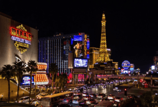 Das Bild zeigt eine Straße mit dichtem Straßenverkehr, hohe Gebäude und Casinos in Las Vegas bei Nacht.