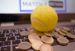 Ein Tennisball sowie verschiedene Geldmünzen liegen auf der Tastatur eines Laptops.