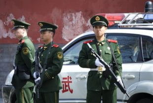 Drei bewaffnete chinesische Polizisten stehen vor einem Polizeiwagen.