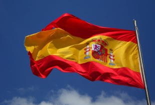 Spanische Flagge vor blauem Himmel und wenigen Wolken im Wind wehend.