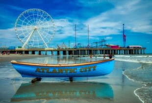 Ein kleines Ruderboot mit der Aufschrift Atlantic City am Strand vor einem Riesenrad.