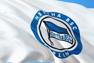 Flagge mit Logo von Hertha BSC im Wind unter blauem Himmel.