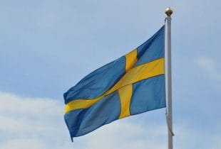 Schwedische Flagge im Wind vor bewölktem Himmel.