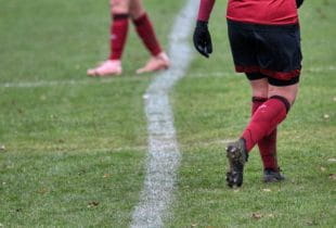 Beine zweier Fußballspieler auf grünem Fußballrasen.