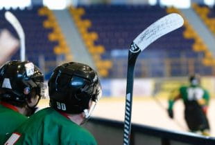 Zwei Eishockeyspieler verfolgen eine Partie vom Seitenrand.