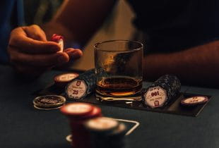 Ein Mann sitzt mit Jetons und einem Glas Scotch am Pokertisch.